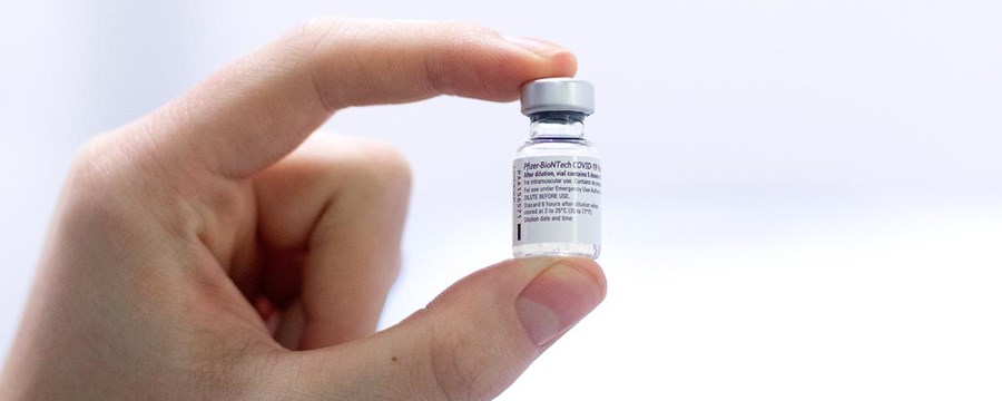 Hånd, der holder COVID-19 vaccine i et lille glas