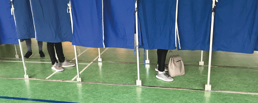 Stemmebokse, hvor man bag gardinerne kan se fødderne af vælgere, der afgiver deres stemme.